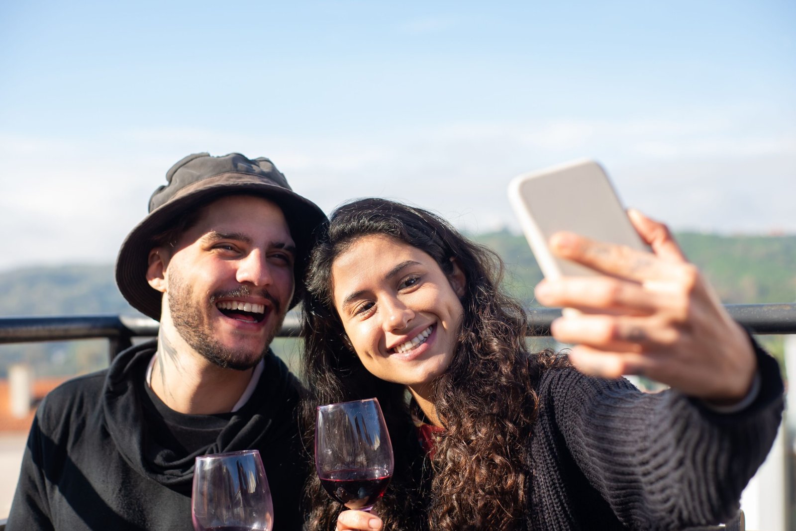 Smiling couple enjoying wine and taking a selfie outdoors in Portugal.